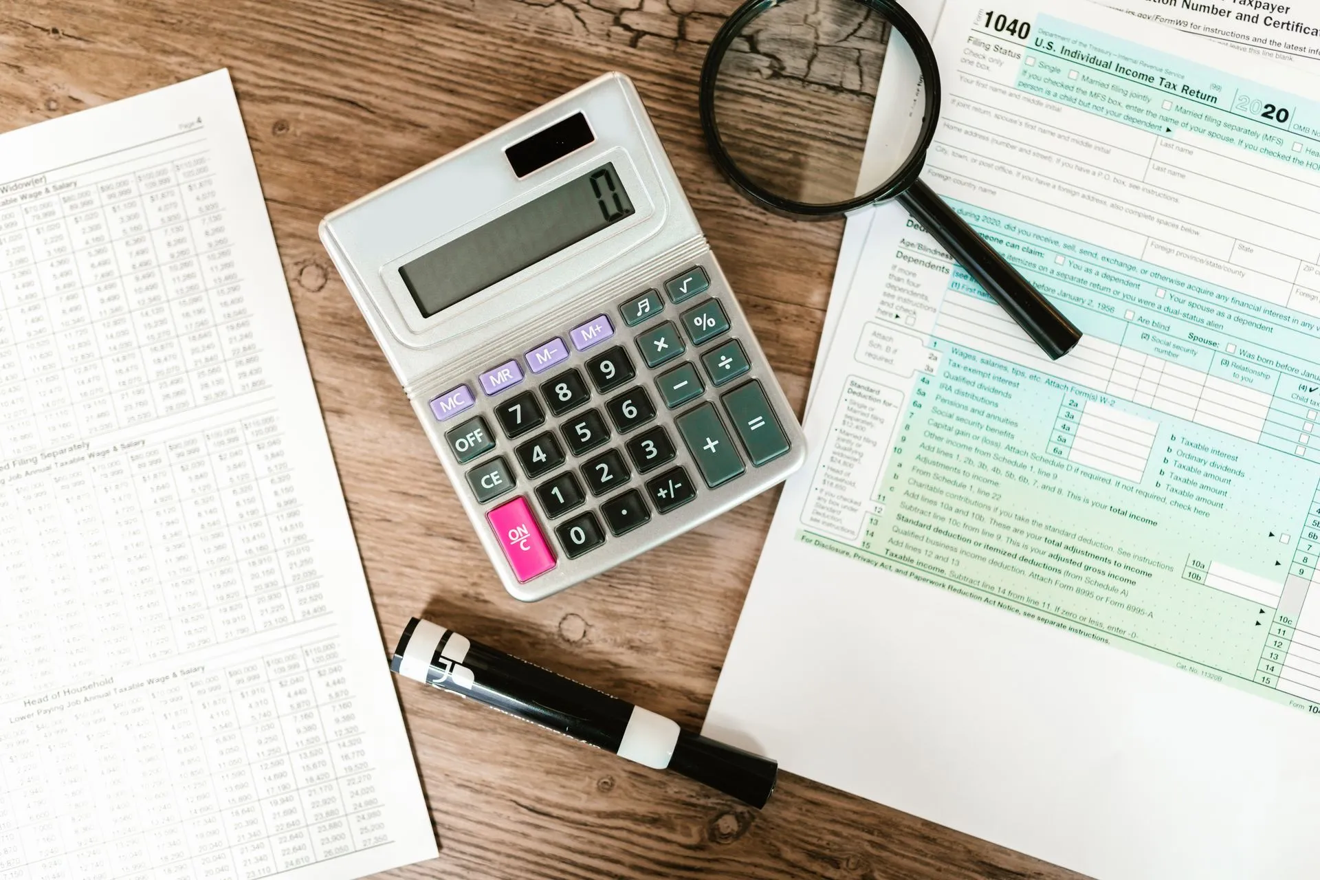 Top view of tax forms, a calculator, and a magnifying glass on a wooden surface, ideal for accounting themes, illustrating Plaid launches LendScore 2 and new fraud and payment risk
