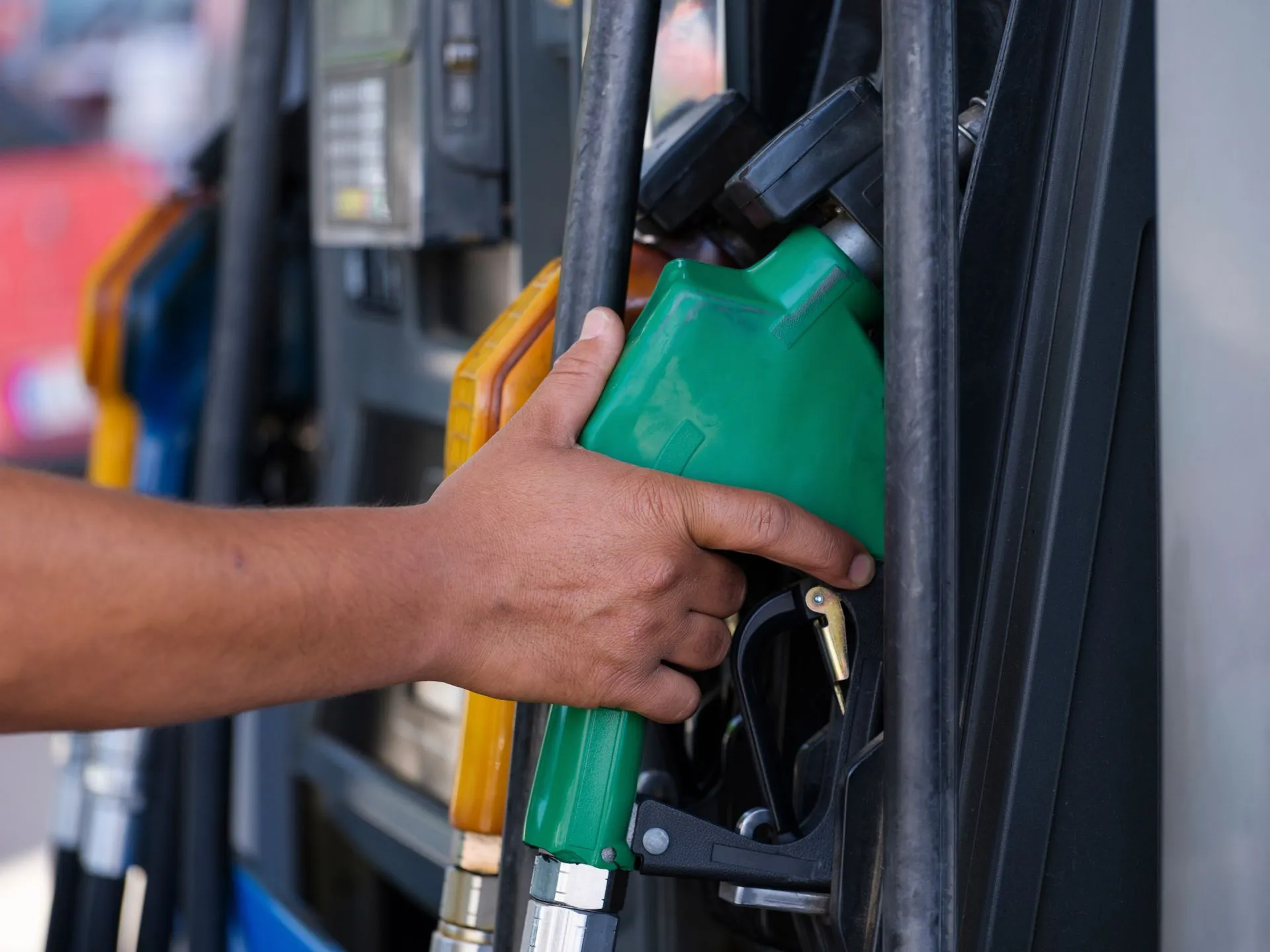 Close-up of a hand holding a green fuel nozzle at a gas pump station outdoors, illustrating Toast adds fuel payments as POS hardware discounts spread and Nayax closes $350M IPS deal
