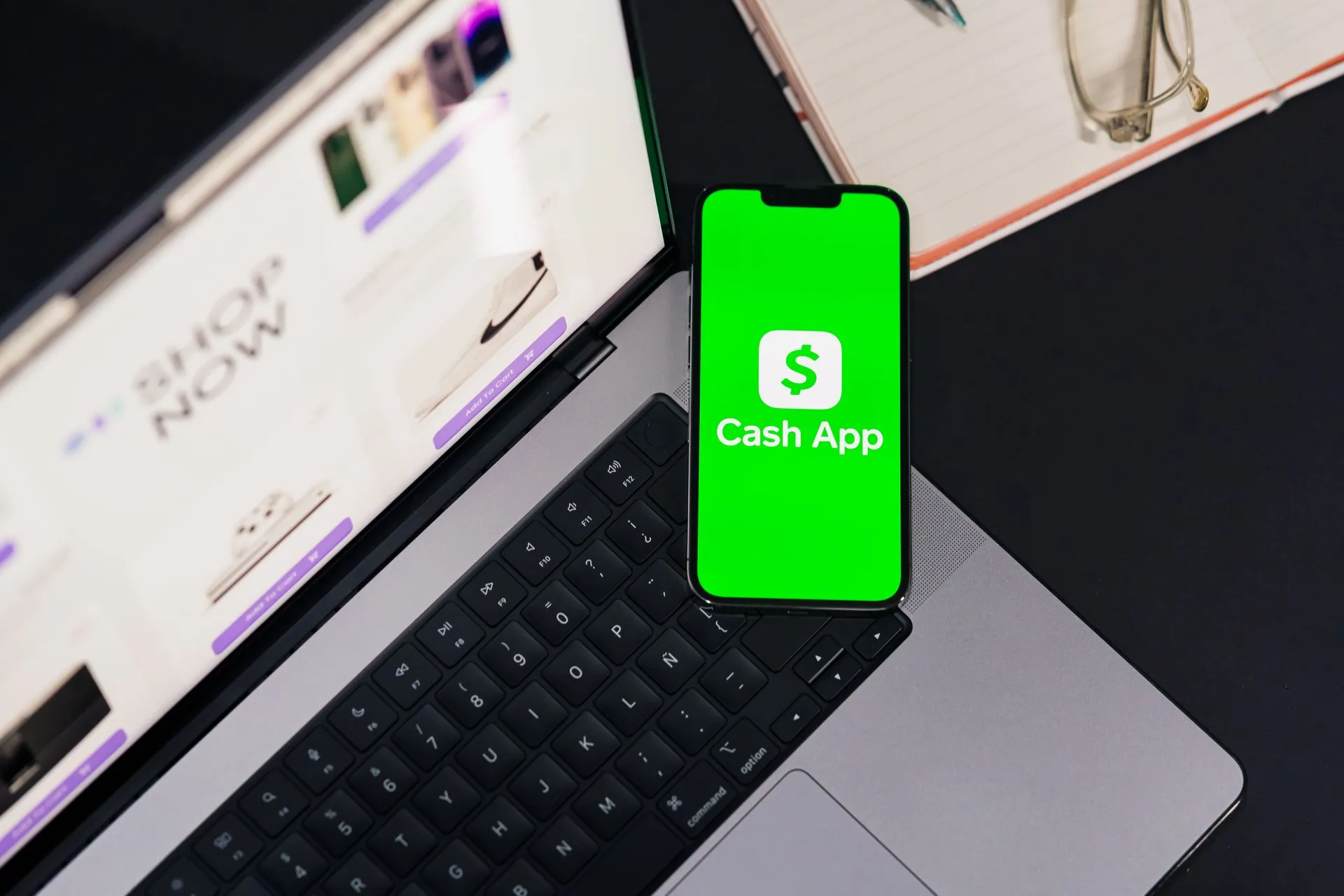 Smartphone showing Cash App screen on laptop keyboard, next to glasses and notebook, illustrating Prometeo account verification now spans 110+ countries as fraud targets 76% of firms