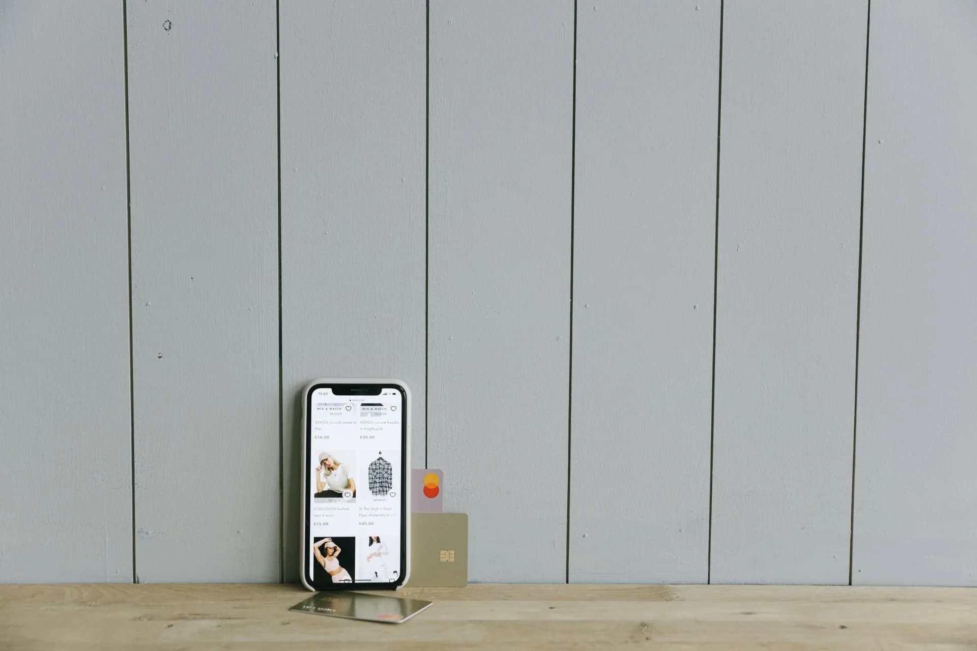 A smartphone displaying an ecommerce site with a credit card, set on a wooden surface, depicting online shopping, illustrating RatHat Android banking trojan's console uses Gemini to rank