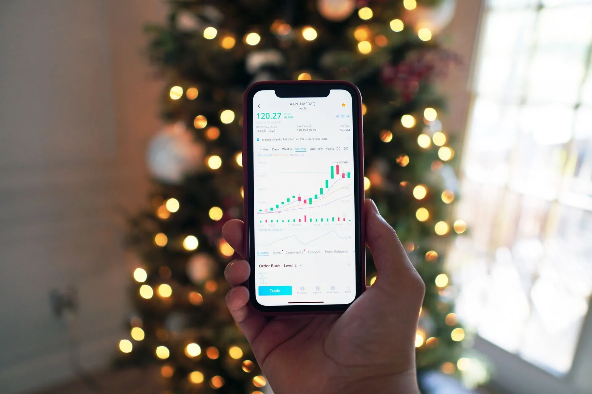 Close-up of a smartphone displaying stock market trading app with a background of Christmas lights, illustrating Robinhood Agents can trade for customers, who can switch off per-order