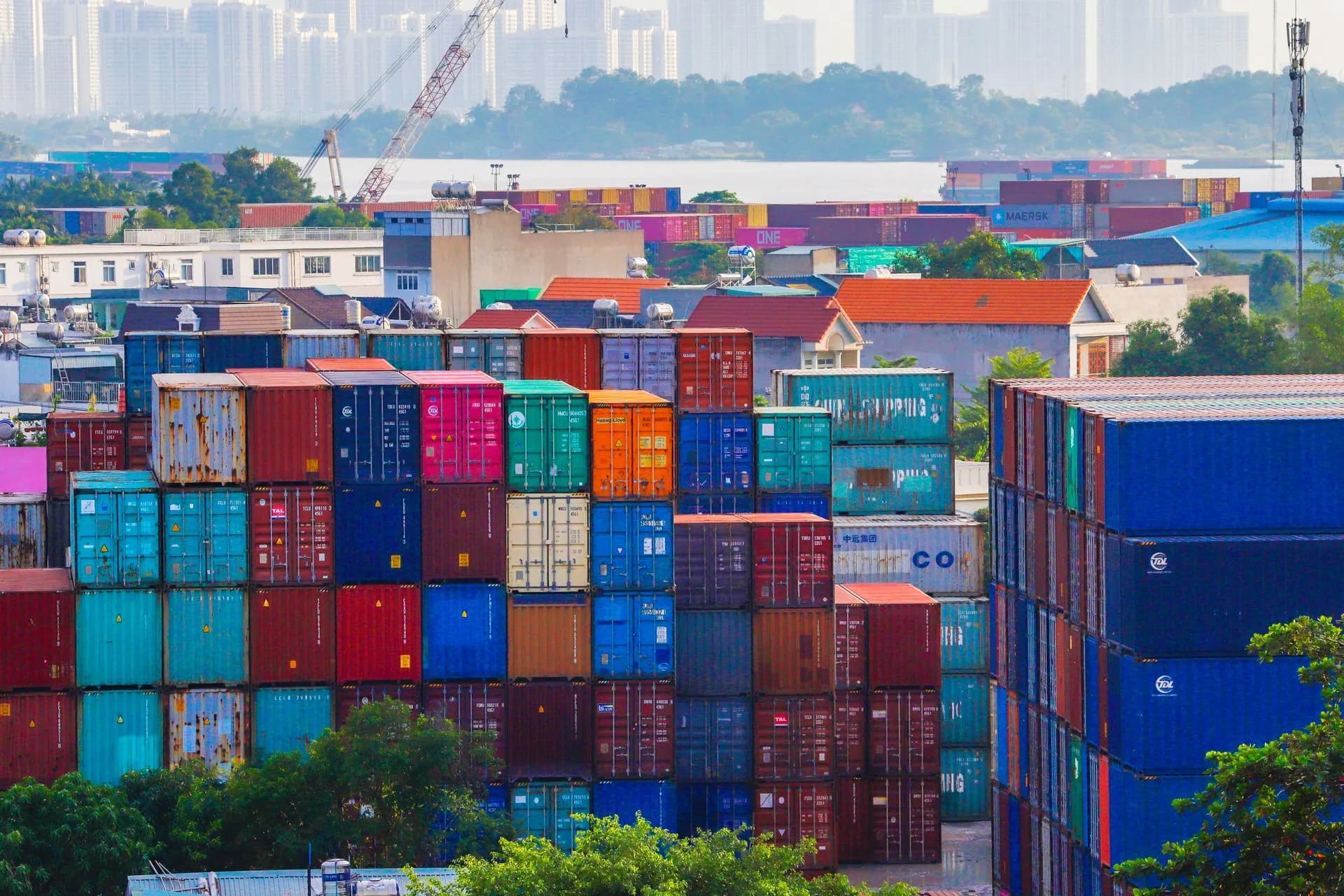 Vibrant stacked cargo containers at a bustling port with urban skyline in background, illustrating SAIC wins $742 million CBP contract to run systems that size up who and what enters