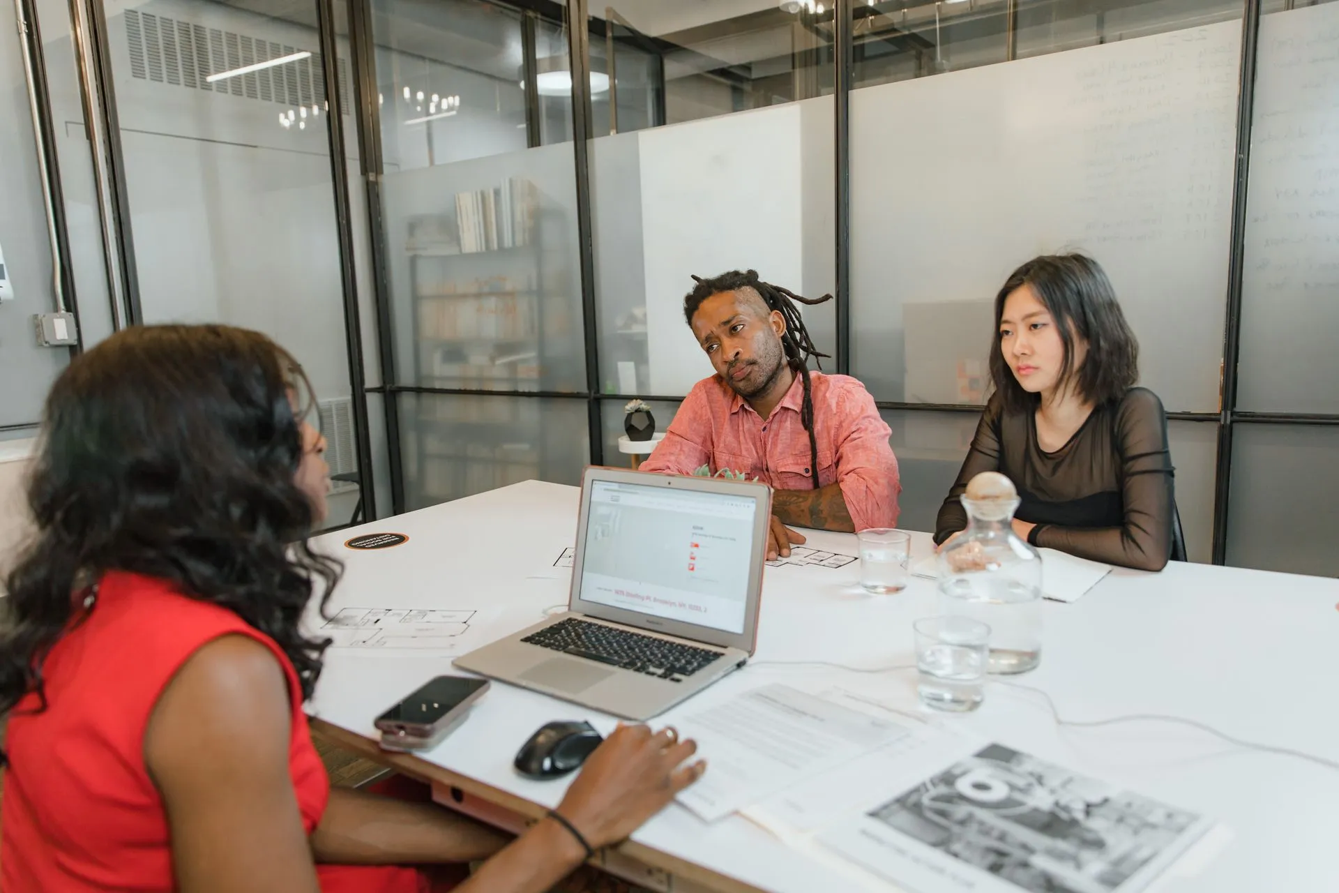 Three professionals engage in an office meeting with a laptop, documents, and discussions, illustrating Salesforce Listen Labs acquisition brings AI that simulates customer reactions