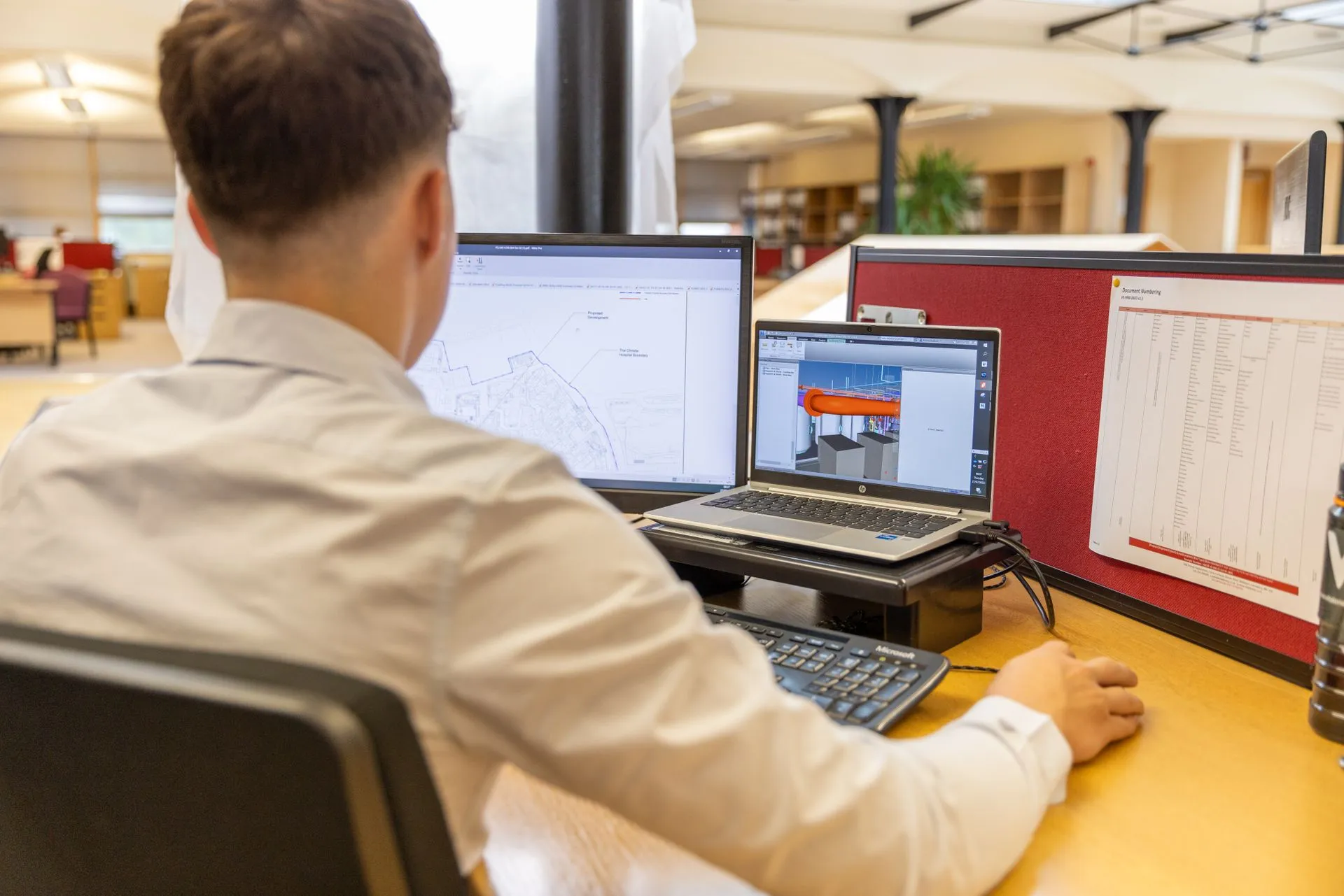 Back view of engineer focused on CAD design at dual monitors in bright office setting, illustrating Schneider Electric to buy PTC for $205 a share, a $23.7 billion enterprise value