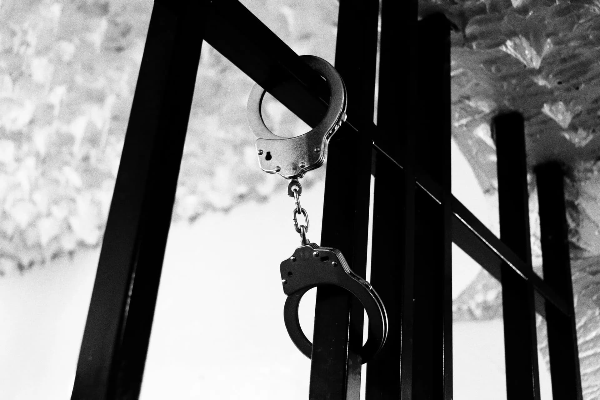 Black and white photo of handcuffs on steel bars, depicting confinement theme, illustrating FBI confirms multiple ShinyHunters arrests as alleged member Rey reportedly aids probe