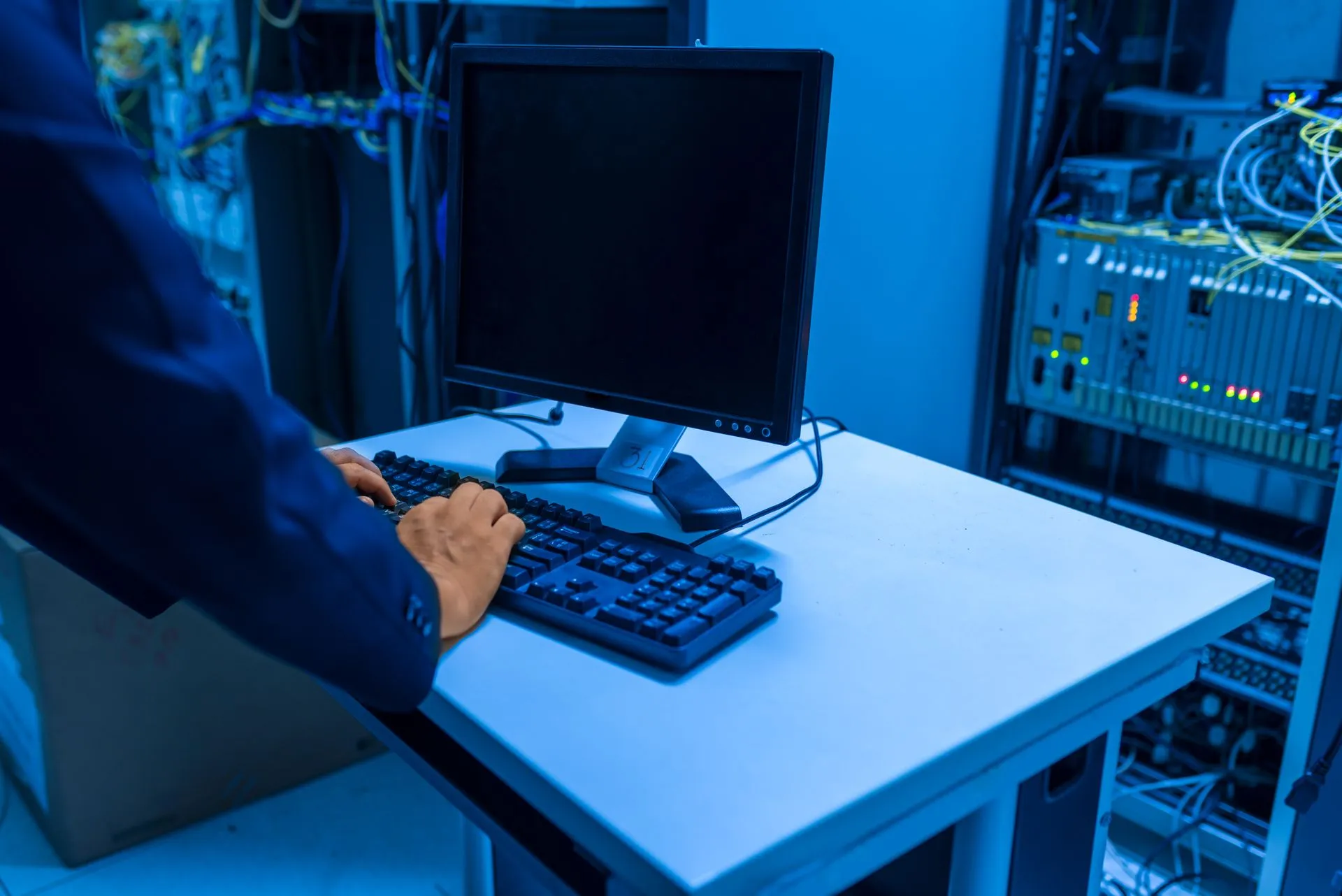 An IT professional operates a computer in a server room, managing network systems and connected devices, illustrating ShinyHunters extortion rolls on despite a Dutch arrest as Mandiant