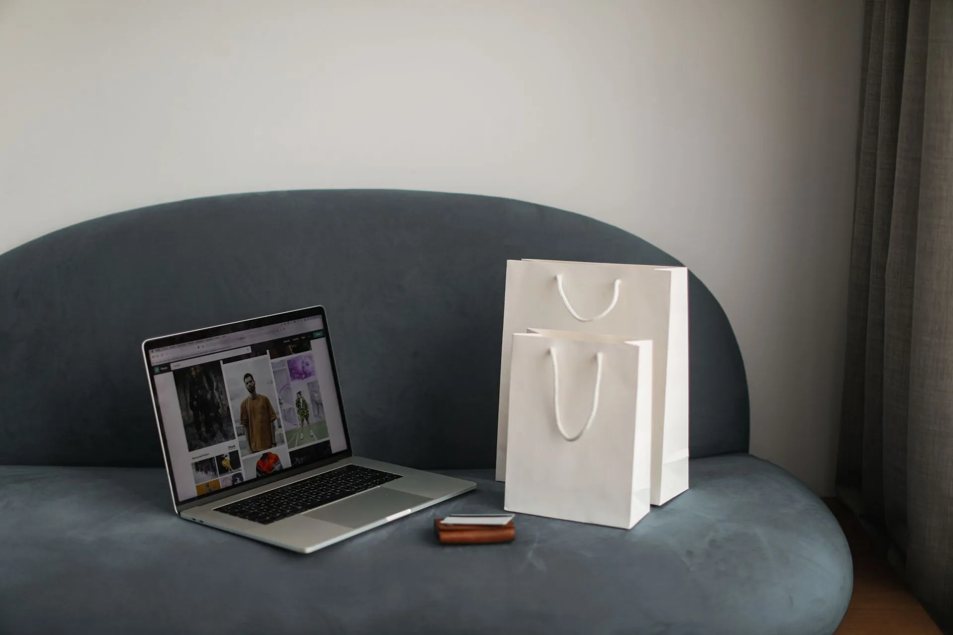 Online shopping setup with a laptop and shopping bags on a stylish couch, illustrating Shopify Canvas lets merchants build stores by chatting with Sidekick, in about 20 minutes