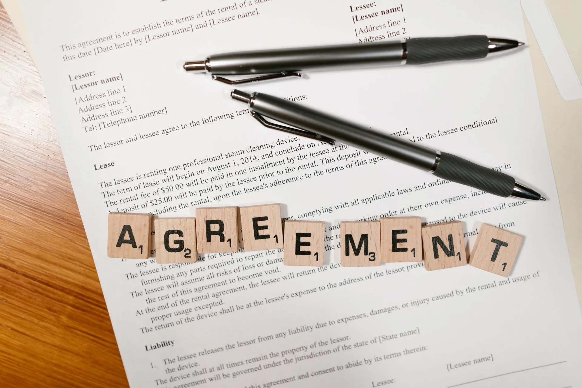 A document with Scrabble tiles spelling 'AGREEMENT' and two pens, symbolizing contract signing, illustrating Software renewal negotiations
