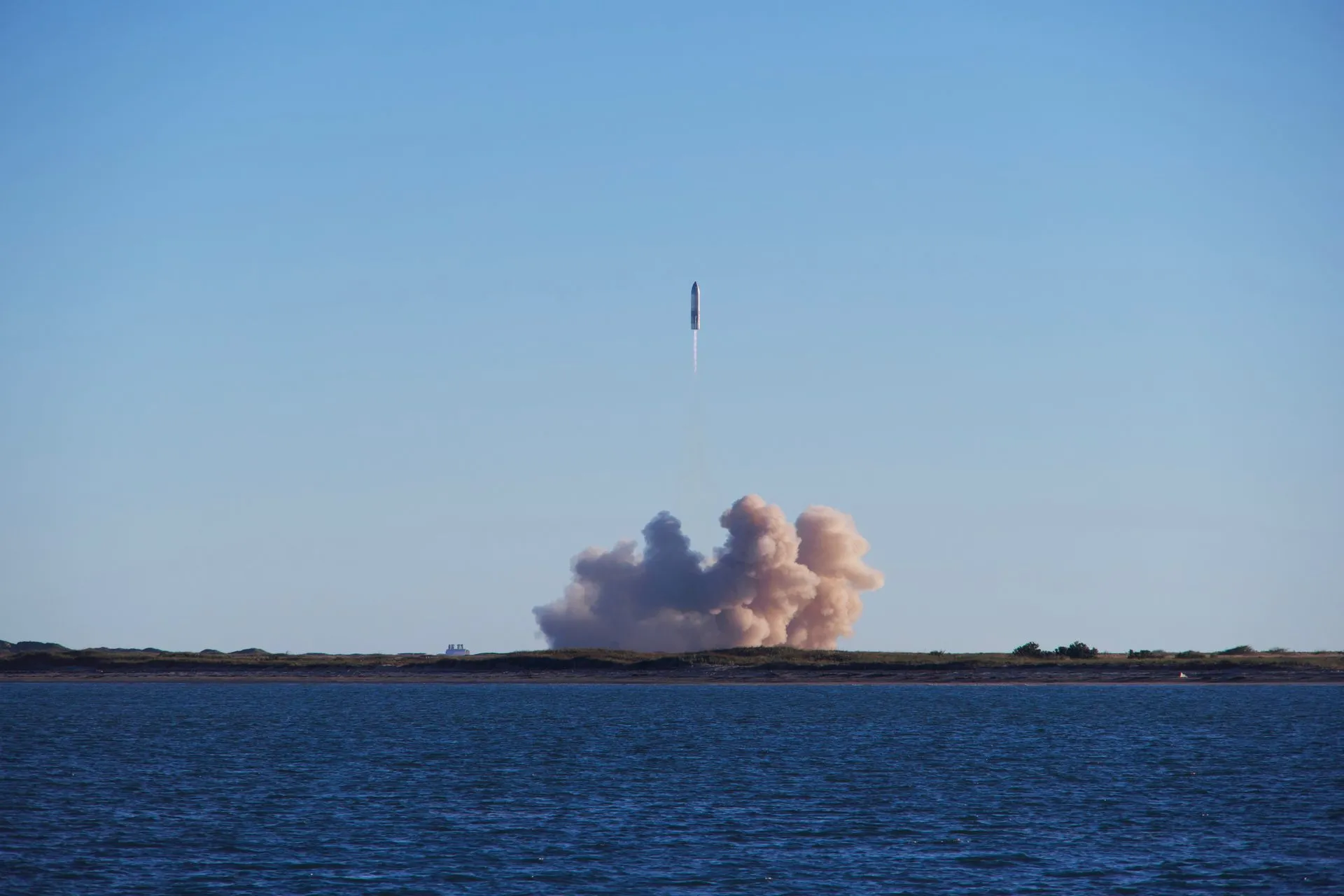 A rocket launch with smoke trails over South Padre Island, viewed across the ocean, illustrating SpaceX Crew-13 docks at the space station in 7 hours 55 minutes, a US record