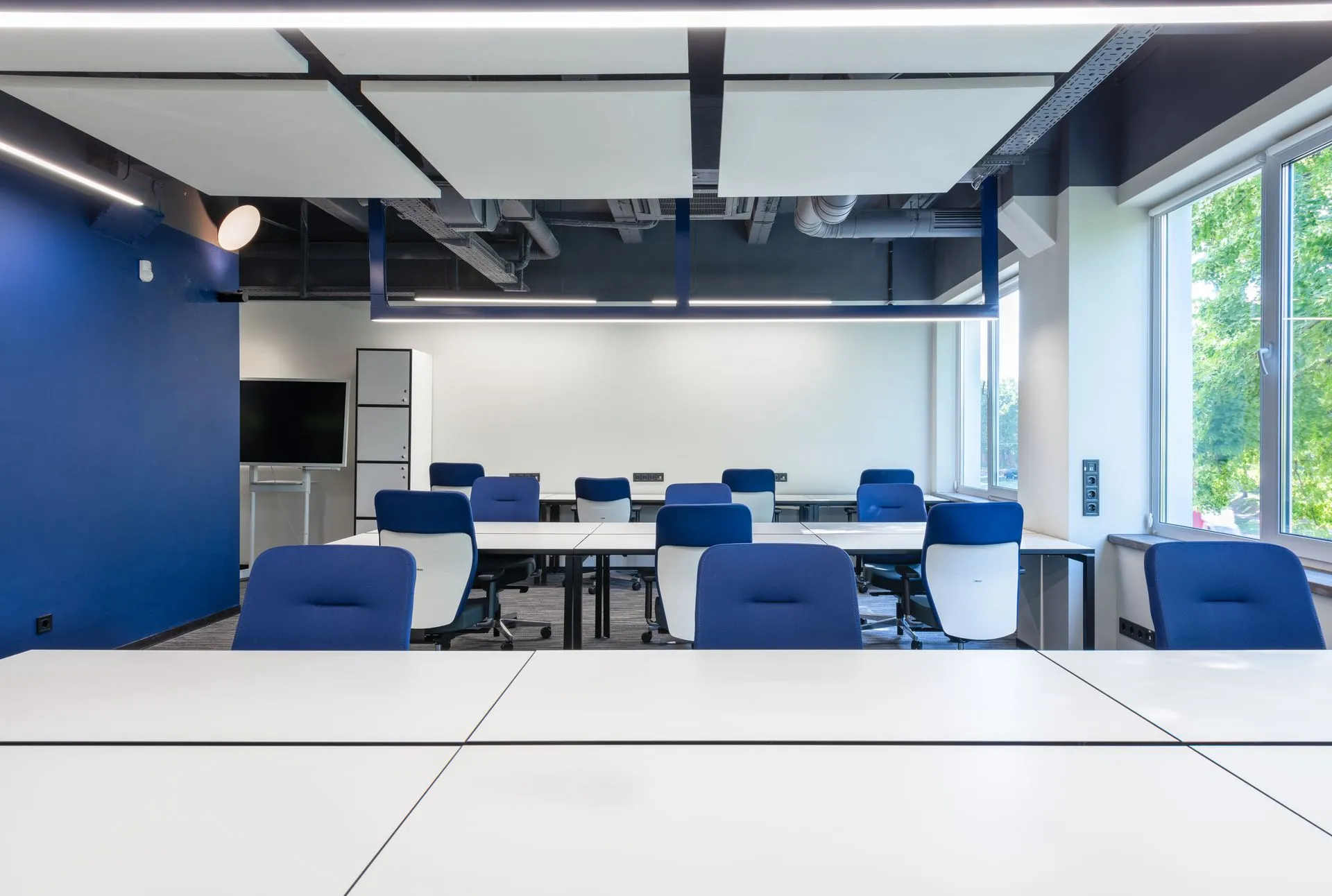 Various white desks with blue chairs placed in modern spacious workspace with big window and monitor in contemporary business, illustrating Supabase raises $150 million led by GIC and acquires Turso