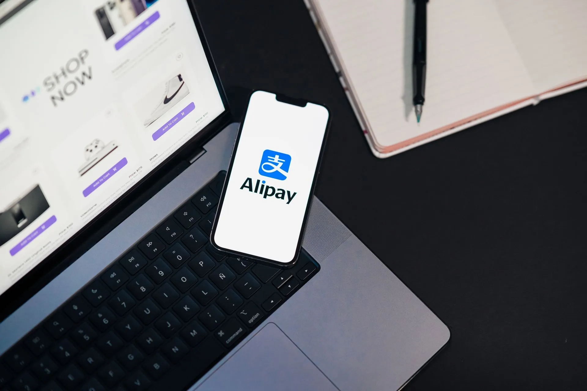 Smartphone displaying Alipay app on open laptop with online shopping site, illustrating Swift cross-border payments plan would let consumers pay abroad with a phone number