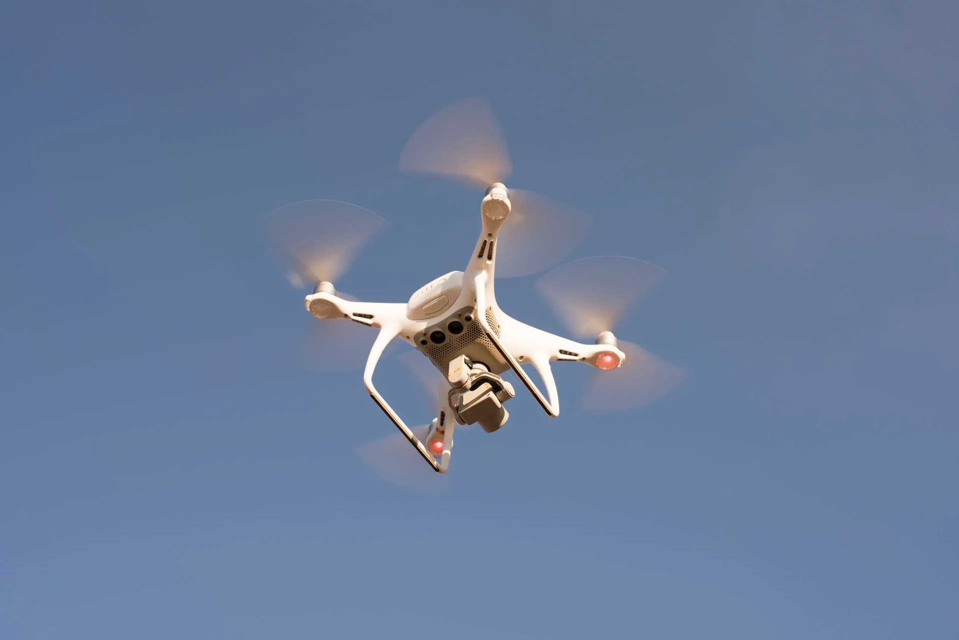 A white drone in flight against a clear blue sky, capturing aerial footage with precision.