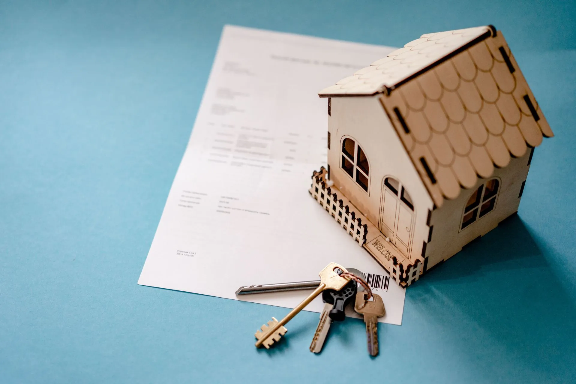 Miniature wooden house with keys and contract symbolizing real estate transactions, illustrating Vesta raises $30M as mortgage lenders put AI agents to work on loan origination