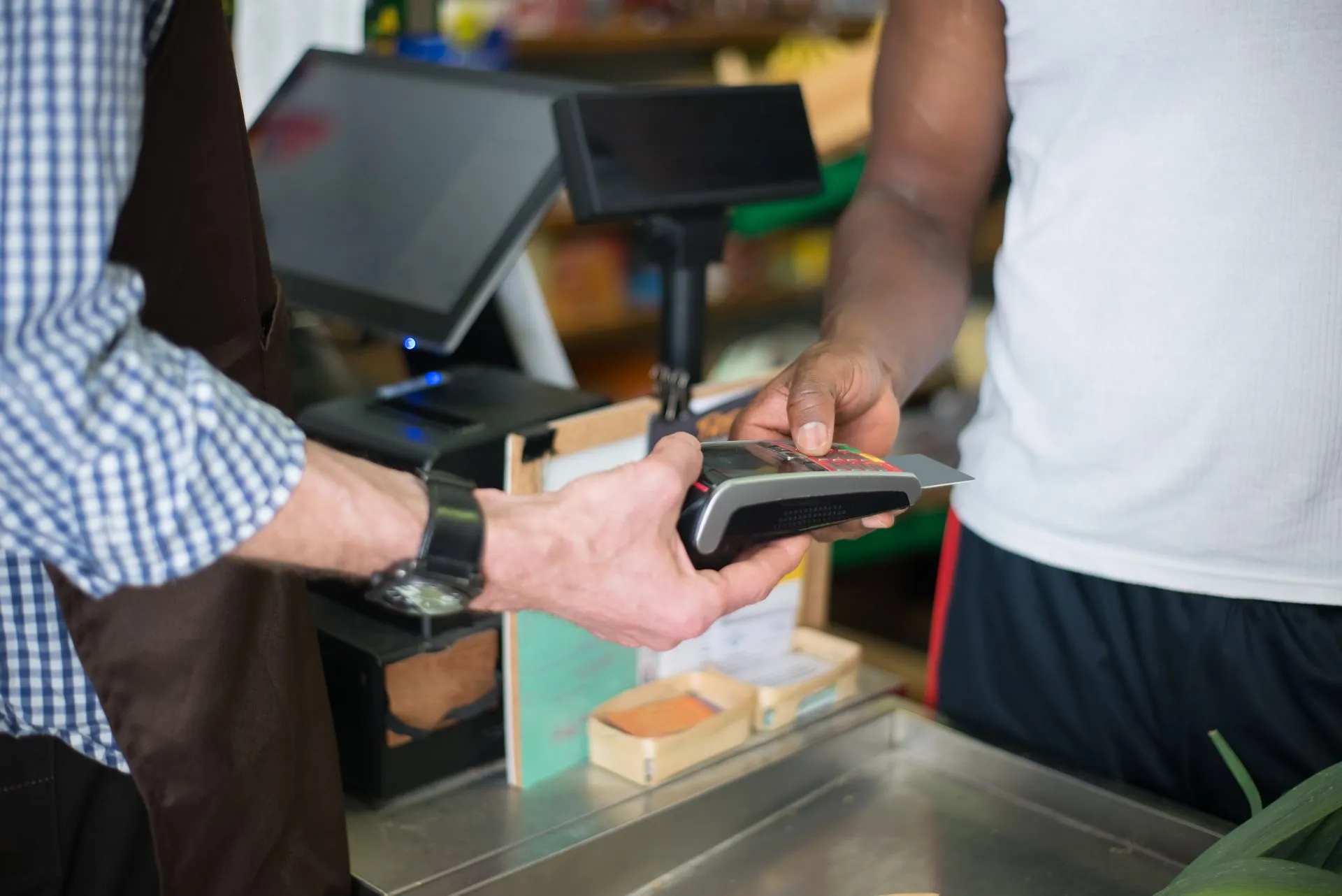 A customer making a payment with a credit card at a store checkout counter using a card reader, illustrating Visa-Mastercard swipe fee settlement draws objections from 978 merchants