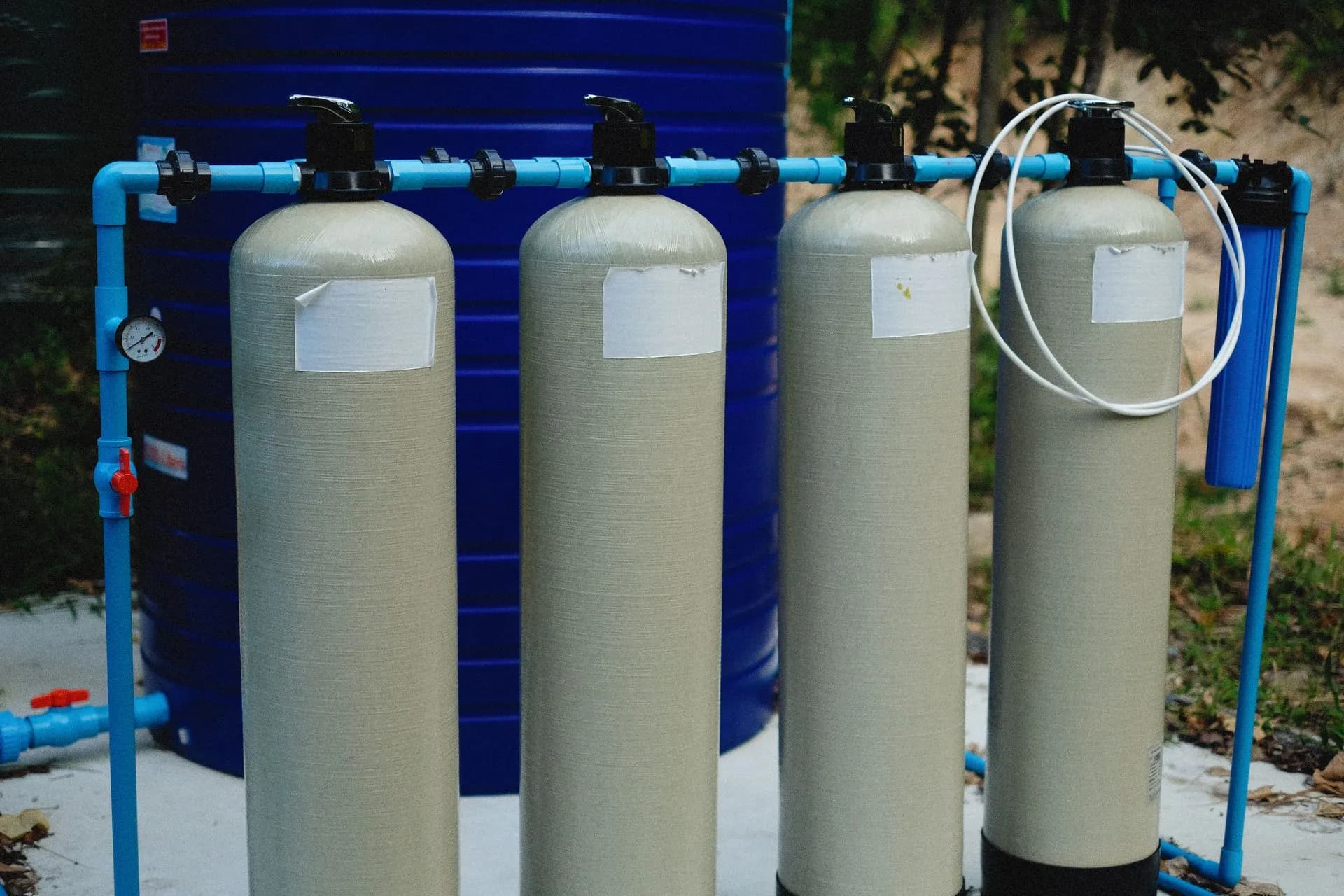 Four beige tanks in an outdoor water treatment setup with blue piping, illustrating Warlock ransomware hits water utility and telecom provider via SharePoint, Symantec says