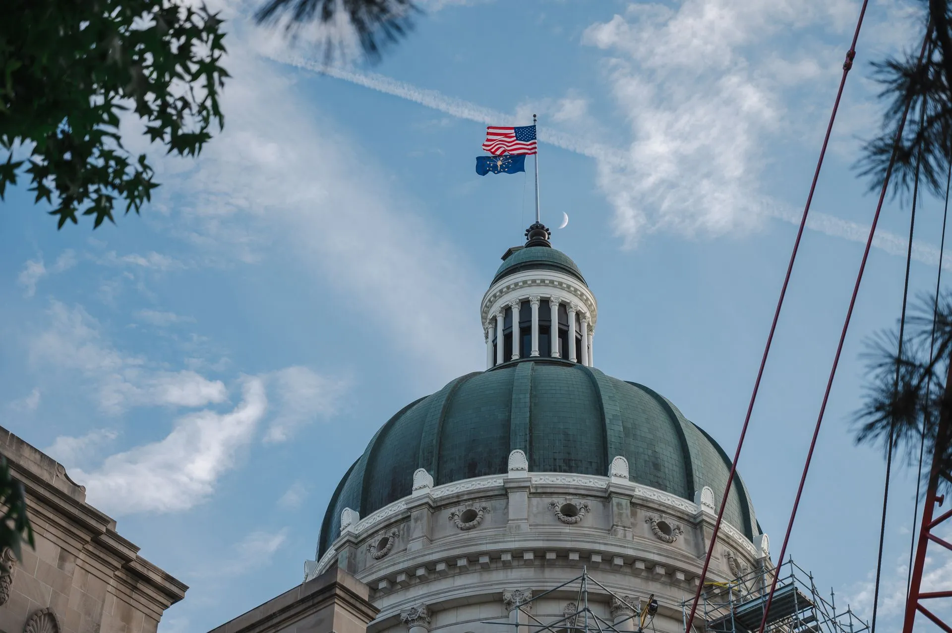 The Indiana State Capitol dome with American and Indiana flags flying against a bright blue sky, illustrating Maryland's Wes Moore forms bipartisan governors group to draft state AI