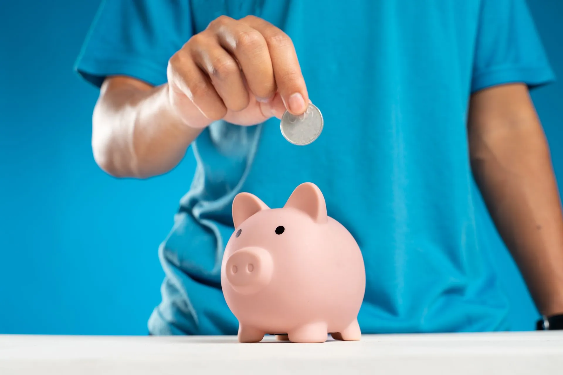 A close-up of an adult's hand dropping a coin into a piggy bank, symbolizing savings and investment, illustrating Workday Total Benefits puts health, wealth and wellbeing perks in one